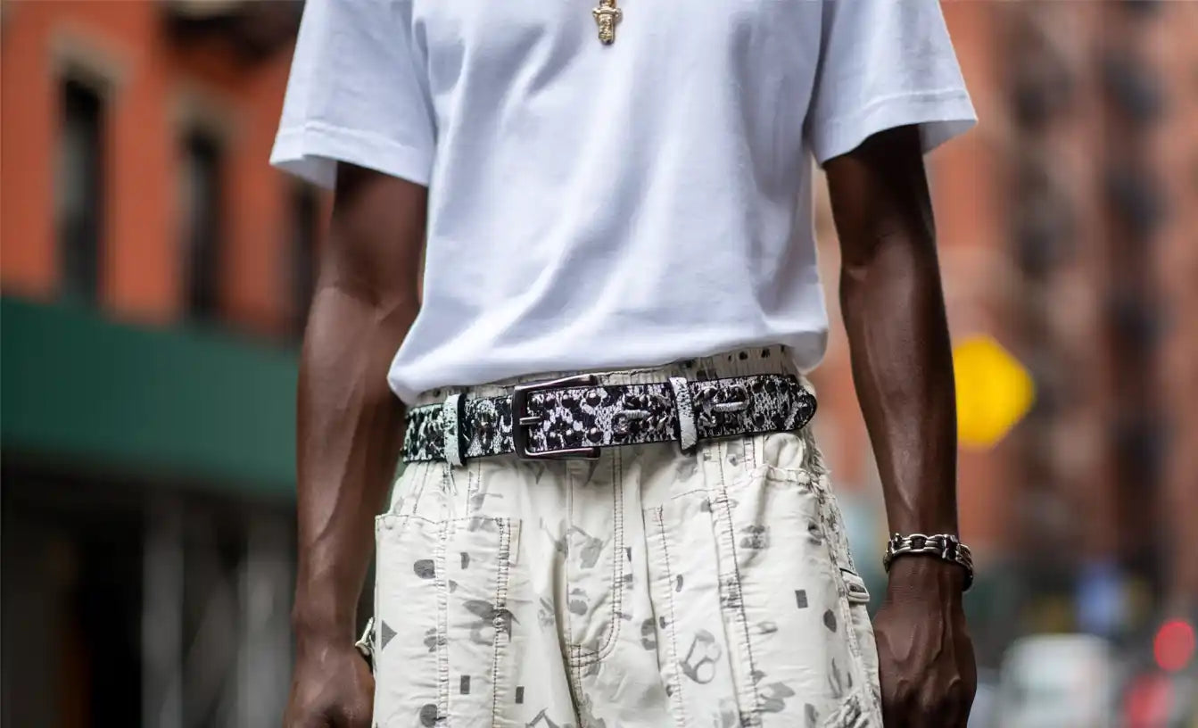 A person in a white t-shirt and patterned shorts wears a black and white patterned studded belt.