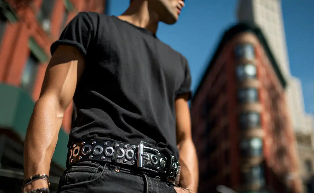 A person in a black t-shirt and black jeans wears a black studded belt with large eyelets.