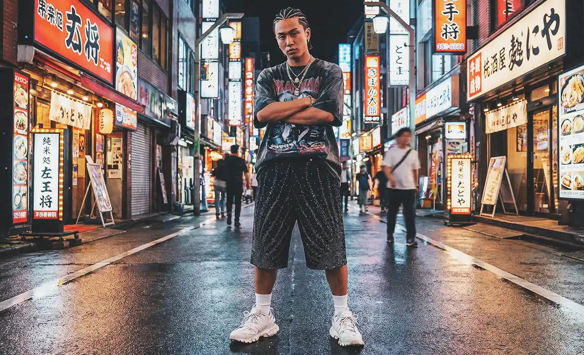 A man standing in a neon-lit city street wearing black Rhinestone Jorts designed with sparkling vertical lines.