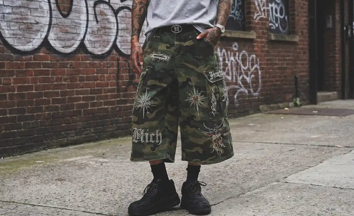 A close-up of camo cargo Rhinestone Jorts decorated with sparkly starburst patterns and gothic lettering.