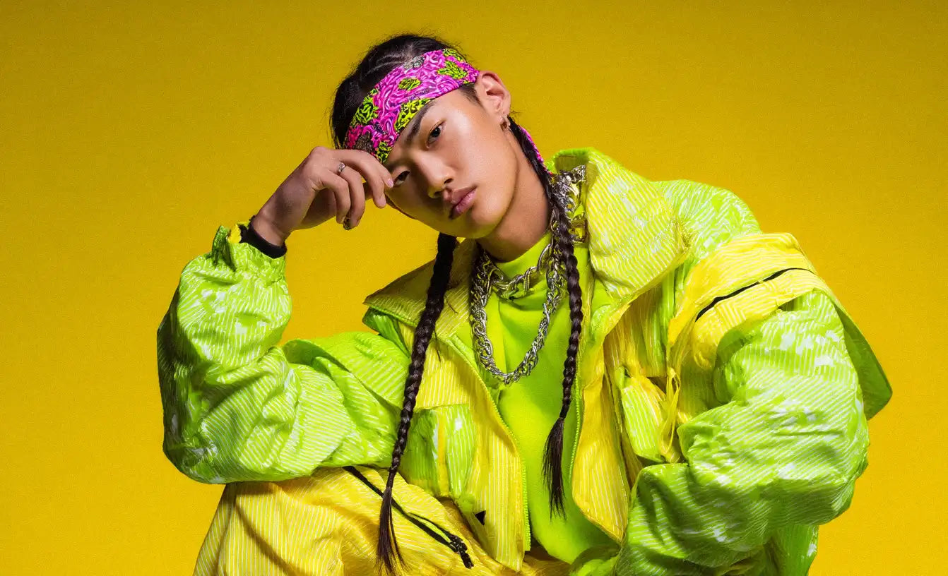 Man dressed in a neon yellow windbreaker and matching pants, accessorized with chains and a pink headband, showcasing eye-catching Y2K fashion with rave-inspired flair.