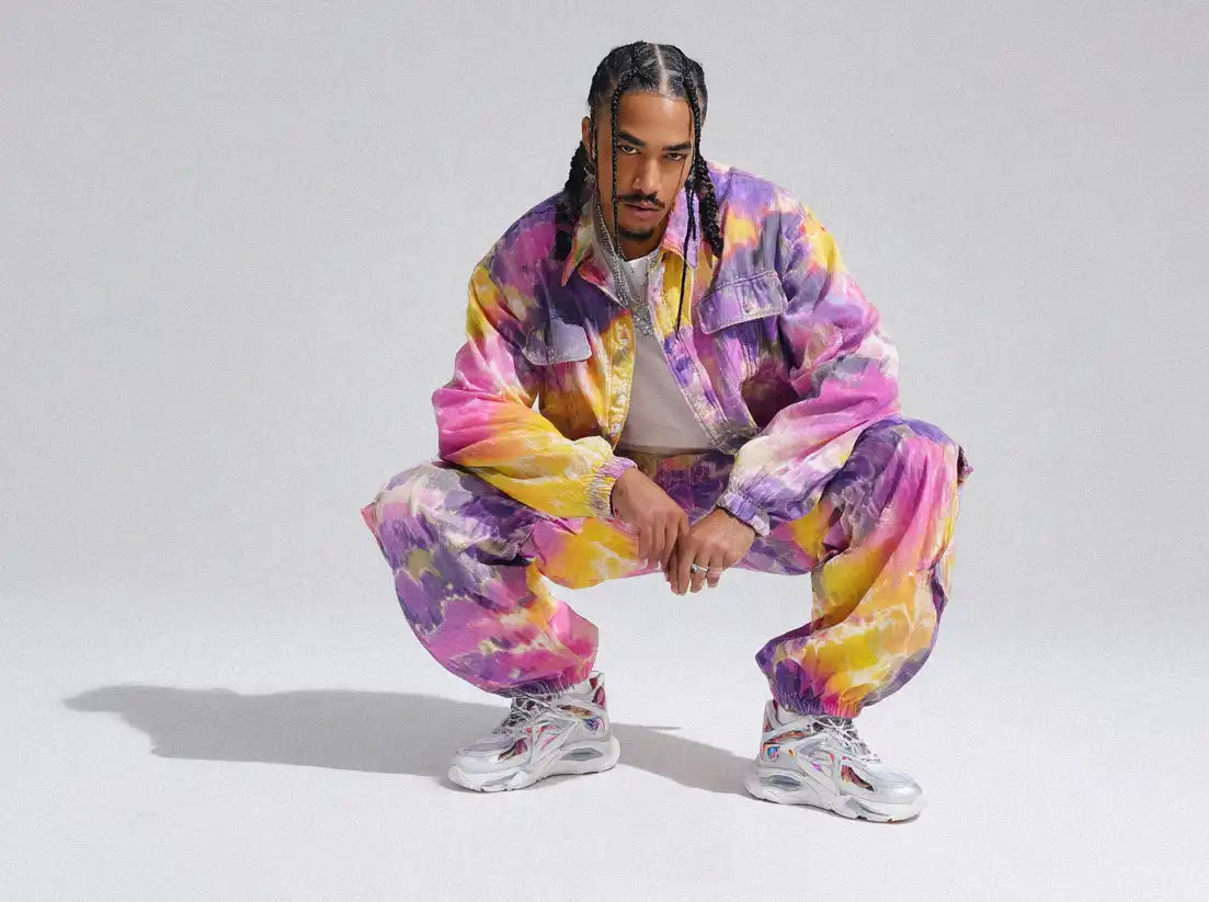 Man crouching in tie-dye pink-and-yellow tracksuit and chunky runners, embodying playful Y2K streetwear style.