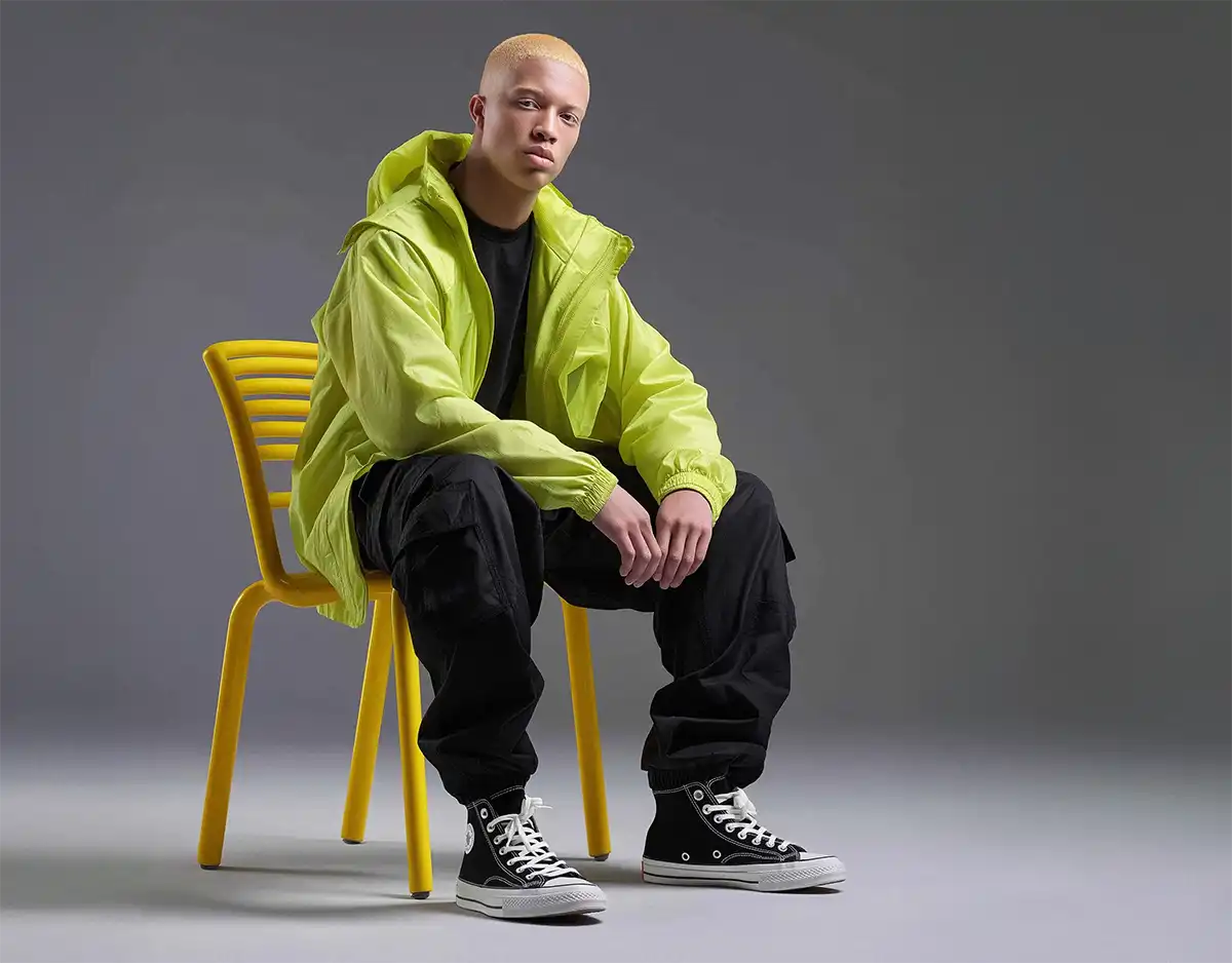 Man with platinum buzz cut in neon windbreaker and black cargo pants, showcasing minimalist Y2K fashion.
